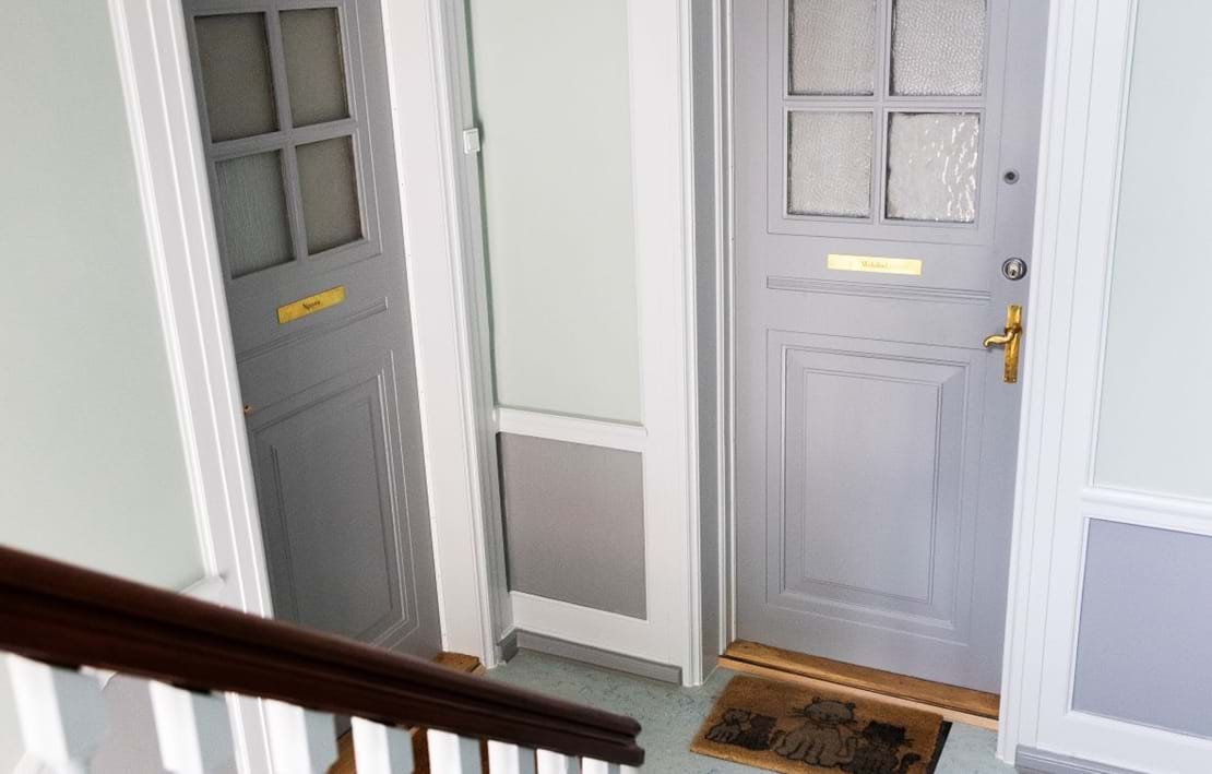 Dørene på hovedtrapperne er malet i en grålig farve, der komplimenterer den lyse væg.
Nye dørhåndtag og navneskilte pryder dørene.